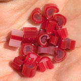A hand holding a collection of small, heart-shaped pieces of red and pink candy.