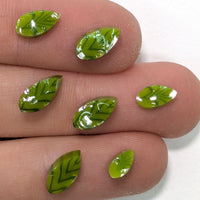 A close-up image of a person's fingers holding several small, green leaf-shaped objects.