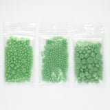 Three clear plastic bags filled with green beads are arranged in a row.