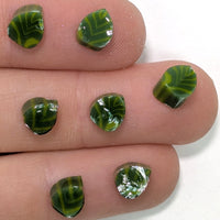 A close-up image of a person's fingers holding small, green leaf-shaped objects.