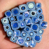 A hand holding a collection of blue and white glass beads or stones, with various shapes and sizes.