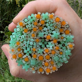 A hand holding a circular arrangement of multicolored flower-shaped objects, including shades of green and orange.
