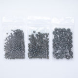 Three transparent plastic bags filled with small gray beads are arranged in a row.