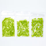 Three transparent plastic bags filled with green beads or objects are arranged in a row.