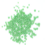 a large pile of small, round, green beads scattered on a white background.