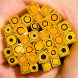 A hand holding a collection of yellow and black geometric shapes, which appear to be a variety of beads or small decorative objects.