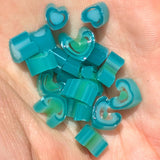 A hand holding a collection of small, colorful heart-shaped objects made of a translucent material, possibly glass or plastic.