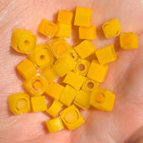 a hand holding a collection of small, yellow, square-shaped objects that appear to be made of a material similar to beads or small plastic pieces.