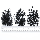 three piles of black beads, each with a ruler placed between them. The ruler is marked with measurements in inches, indicating the size of the beads.