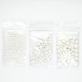 three transparent plastic bags filled with white beads or small white objects, arranged in a row.