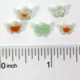 a collection of small, colorful butterfly-shaped objects, possibly made of glass or plastic, placed next to a ruler for size comparison.