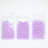 Three clear plastic bags filled with small, round, purple beads are arranged in a row.