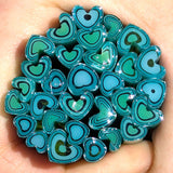 A hand holding a collection of small, colorful heart-shaped objects in shades of blue and green.