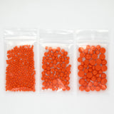 Three clear plastic bags filled with orange beads are arranged in a row.