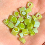 A hand holding a collection of green, square-shaped objects resembling small pieces of celery or similar vegetables.