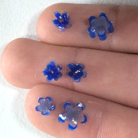 a close-up view of a person's fingers, with small blue flower-shaped objects placed on the skin.