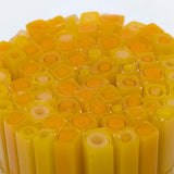 The image is a close-up of a collection of yellow and orange cylindrical objects, possibly made of glass or plastic, arranged in a circular pattern.