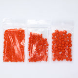 Three clear plastic bags filled with orange beads are arranged in a row against a white background.
