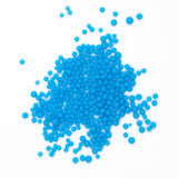 A pile of small, round, blue beads or spheres scattered on a white background.