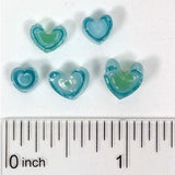 a collection of small, heart-shaped objects made of blue and green materials, with a ruler for scale.