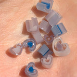 a collection of small, heart-shaped objects made of clear plastic, scattered on a pink surface.