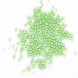 a pile of small, round, green beads or spheres scattered on a white background.