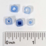 a collection of small blue beads arranged on a white surface, with a ruler for scale.