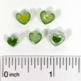 a collection of green heart-shaped objects, possibly made of glass or plastic, arranged on a white surface next to a ruler for size comparison.