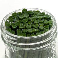 A glass jar filled with green, leaf-shaped objects, possibly herbs or spices.