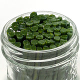 A glass jar filled with green, leaf-shaped objects, possibly herbs or spices.