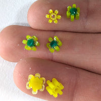 A close-up image of a person's fingers holding small yellow flower-shaped objects with green centers.