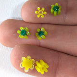 A close-up image of a person's fingers holding small yellow flower-shaped objects with green centers.
