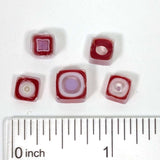 a collection of red and purple glass beads, each varying in shape and size, arranged on a white surface. A ruler is placed next to the beads to provide a scale for size comparison.