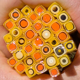 A close-up image of a hand holding a collection of colorful glass beads or glass rods, with a variety of shapes and sizes.