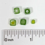 a collection of green glass beads, each varying in size, placed next to a ruler for scale.