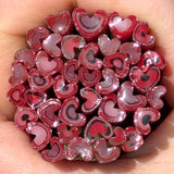 A close-up image of a hand holding a collection of small, heart-shaped objects made of a shiny, metallic material.