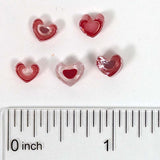 a collection of small red heart-shaped objects, possibly beads or buttons, arranged on a white surface next to a ruler for size comparison.