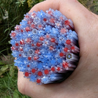 A hand is holding a large cluster of colorful plastic straws, with red and blue plastic flowers attached to them.