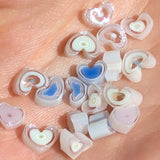 a collection of small, heart-shaped objects made of glass or plastic, scattered on a surface.
