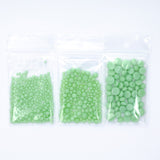 Three transparent plastic bags filled with green beads are arranged in a row.