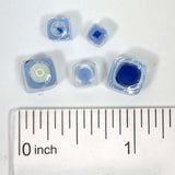 a collection of blue and white glass beads or stones, each varying in size, placed next to a ruler for scale.