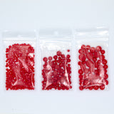 Three clear plastic bags filled with red beads are arranged in a row on a white background.