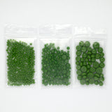 Three transparent plastic bags filled with green objects, likely pills or capsules, are arranged in a row.