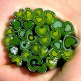 A close-up image of a hand holding a cluster of green and black heart-shaped objects.