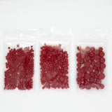 Three clear plastic bags filled with red beads are arranged in a row on a white background.