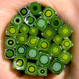a close-up view of a hand holding a collection of green and black glass beads.