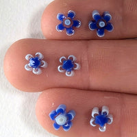 a close-up view of a person's fingers, each adorned with a small blue and white flower-shaped object.