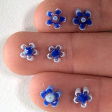 a close-up view of a person's fingers, each adorned with a small blue and white flower-shaped object.