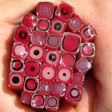 A hand holding a collection of colorful glass beads or stones with various shapes and patterns, including circles, squares, and other geometric designs.