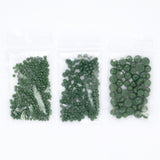 Three transparent plastic bags filled with green beads or buttons are arranged in a row.